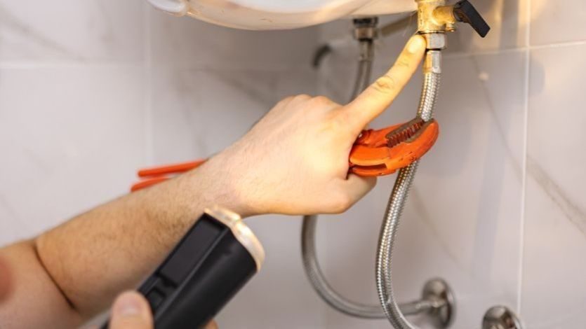 Plumber examining leak underside sink.