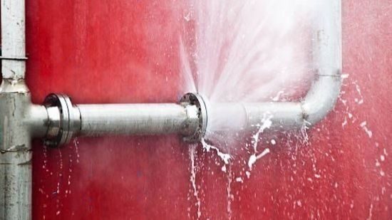 Burst pipe against red wall.