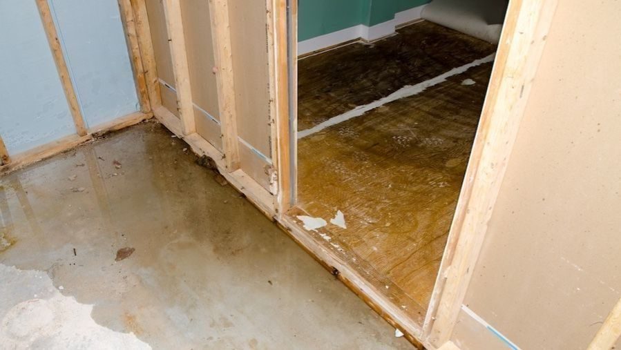 Water damage on a concrete floor and exposed wall framing caused by a residential slab leak requiring professional slab leak repair.