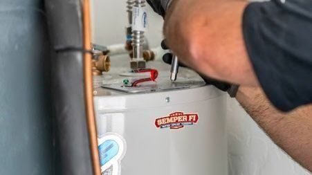 Professional plumber servicing a residential tank water heater during maintenance or repair in a home's utility area.