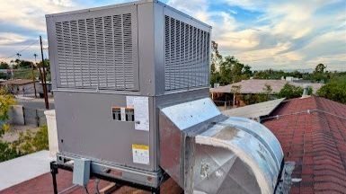 Rooftop HVAC condenser unit with vented housing and attached ductwork on a flat roof, blue sky above.