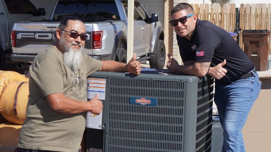 Two HVAC techs resting against an air conditioning unit.